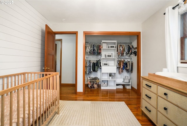 bedroom featuring a closet, a nursery area, wooden walls, and hardwood / wood-style flooring