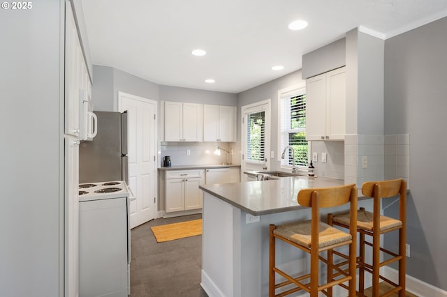 420 S State St, Lake Oswego, OR 97034 - kitchen featuring white appliances, a peninsula, decorative backsplash, white cabinetry, and a kitchen bar