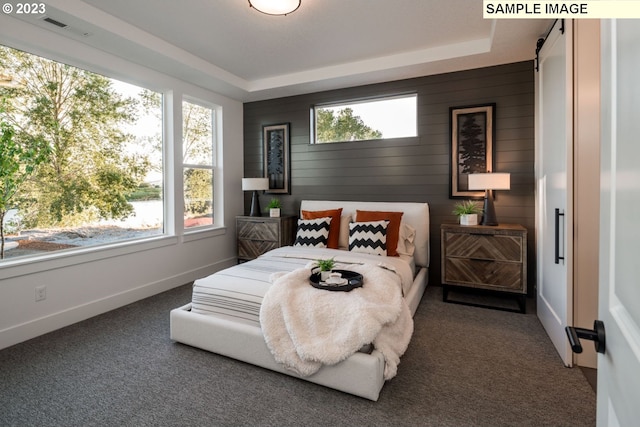 bedroom with a raised ceiling, multiple windows, wood walls, and dark carpet