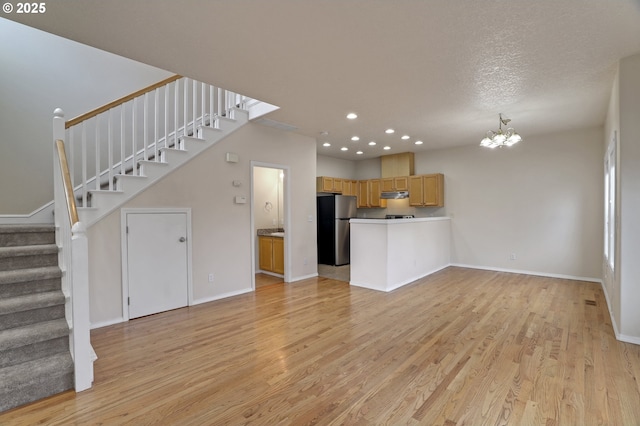 unfurnished living room featuring baseboards, light wood finished floors, an inviting chandelier, recessed lighting, and stairs