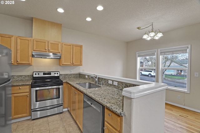 kitchen with a sink, under cabinet range hood, appliances with stainless steel finishes, a peninsula, and a chandelier