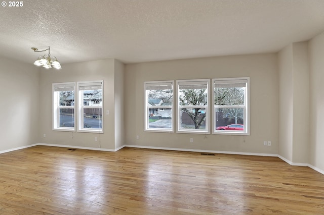 spare room with a textured ceiling, baseboards, light wood-type flooring, and a chandelier