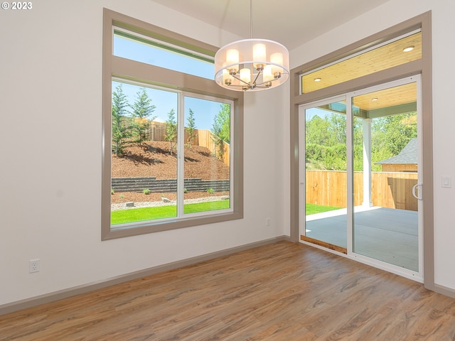 unfurnished room featuring plenty of natural light, a chandelier, and light wood-type flooring