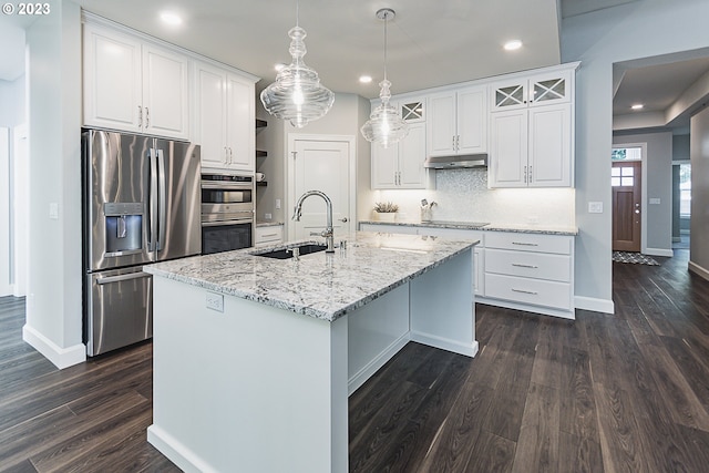 kitchen with hanging light fixtures, appliances with stainless steel finishes, white cabinets, a center island with sink, and dark hardwood / wood-style flooring