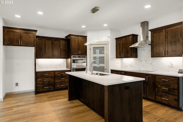 kitchen featuring hanging light fixtures, light wood-type flooring, sink, and wall chimney range hood