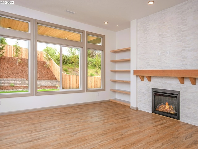 unfurnished living room with a stone fireplace and light wood-type flooring