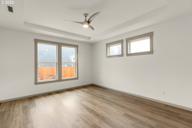 empty room with a tray ceiling, ceiling fan, and light wood-type flooring