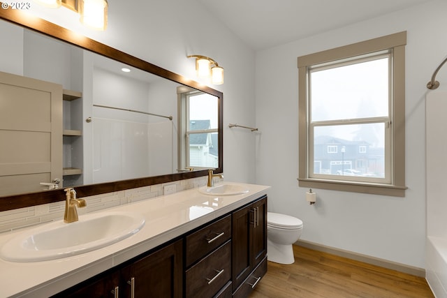 full bathroom with toilet, hardwood / wood-style flooring, washtub / shower combination, tasteful backsplash, and dual bowl vanity