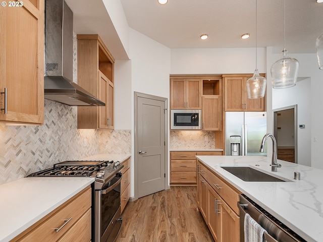 kitchen featuring pendant lighting, stainless steel appliances, tasteful backsplash, light hardwood / wood-style flooring, and wall chimney exhaust hood