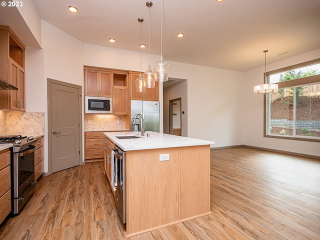 kitchen featuring appliances with stainless steel finishes, light hardwood / wood-style floors, tasteful backsplash, an island with sink, and pendant lighting