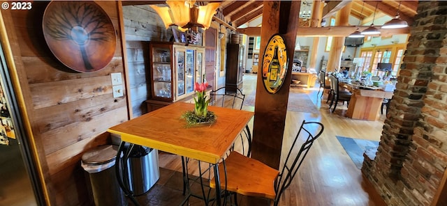 dining room with brick wall, vaulted ceiling with beams, an inviting chandelier, and dark hardwood / wood-style flooring