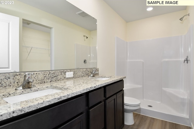 bathroom with toilet, large vanity, a shower, wood-type flooring, and dual sinks