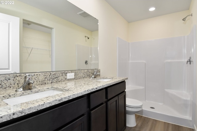 bathroom with a shower, large vanity, dual sinks, toilet, and hardwood / wood-style flooring