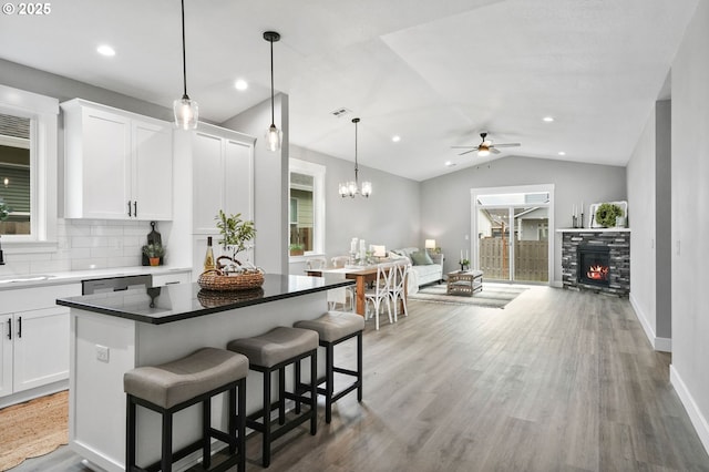 kitchen featuring hardwood / wood-style flooring, a kitchen breakfast bar, a fireplace, white cabinets, and vaulted ceiling