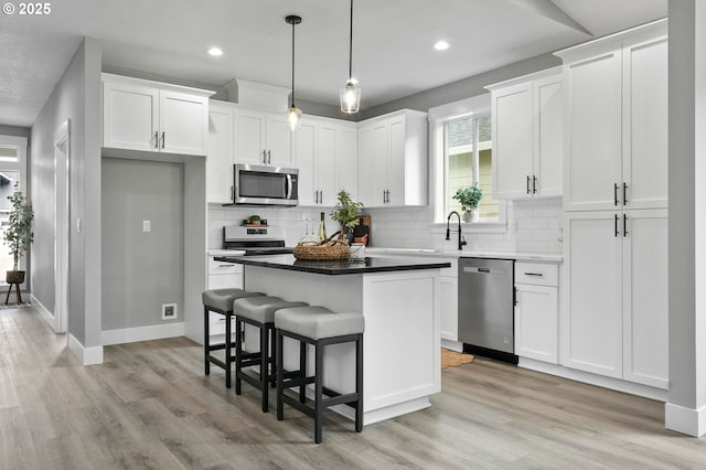 kitchen featuring appliances with stainless steel finishes, white cabinetry, hanging light fixtures, backsplash, and a center island