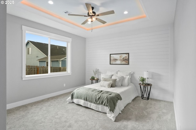 carpeted bedroom with a raised ceiling and ceiling fan