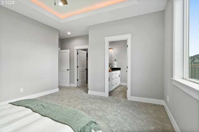 bedroom featuring ensuite bath, a raised ceiling, and light carpet