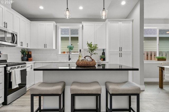 kitchen featuring sink, appliances with stainless steel finishes, white cabinetry, tasteful backsplash, and decorative light fixtures