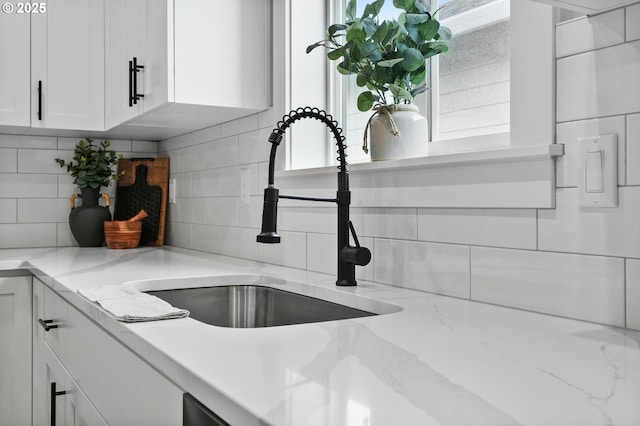 details featuring light stone counters, backsplash, sink, and white cabinets