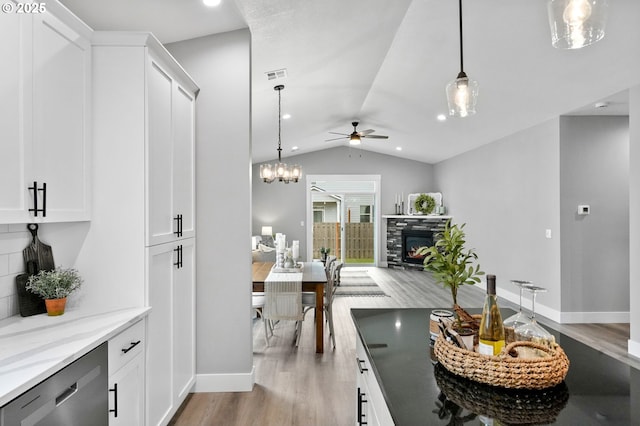 dining room with lofted ceiling, a stone fireplace, ceiling fan with notable chandelier, and light hardwood / wood-style floors