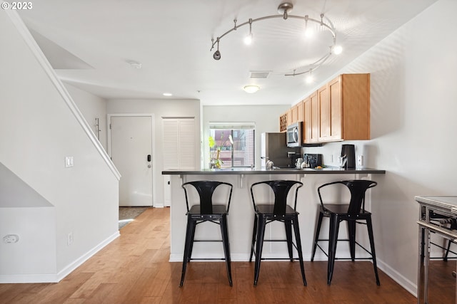 kitchen featuring a kitchen breakfast bar, appliances with stainless steel finishes, light hardwood / wood-style floors, track lighting, and light brown cabinets