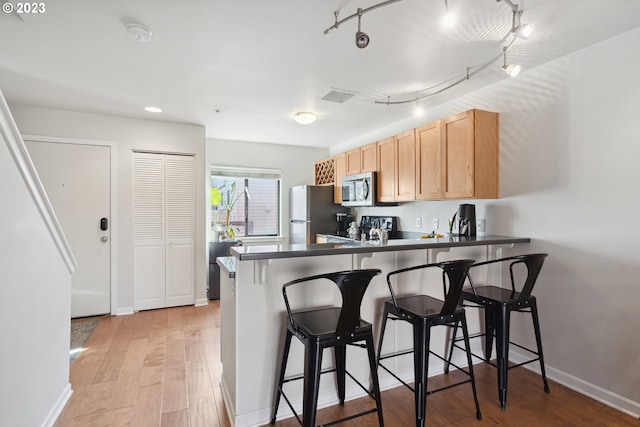 kitchen with a kitchen bar, stainless steel appliances, kitchen peninsula, and light hardwood / wood-style floors