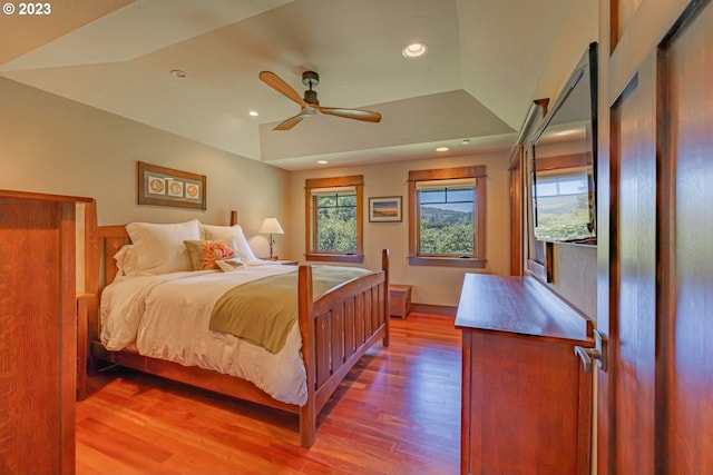 bedroom with hardwood / wood-style floors, ceiling fan, and a tray ceiling