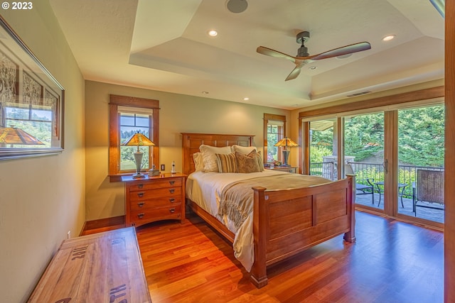 bedroom featuring ceiling fan, access to exterior, dark hardwood / wood-style floors, and a tray ceiling