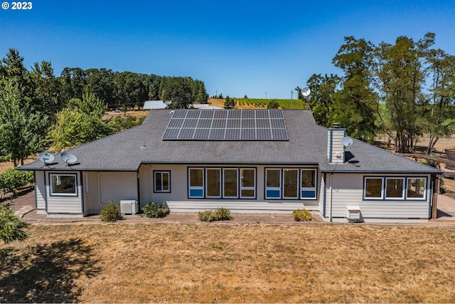 rear view of house featuring a lawn, central AC unit, and solar panels