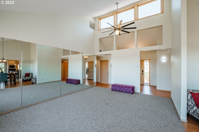 interior space featuring carpet, a healthy amount of sunlight, ceiling fan with notable chandelier, and a high ceiling