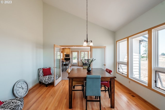 dining area with high vaulted ceiling, a chandelier, and light hardwood / wood-style floors