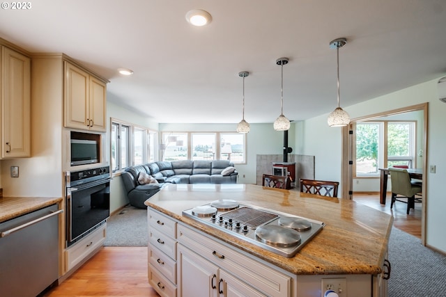 kitchen featuring appliances with stainless steel finishes, pendant lighting, a center island, light stone counters, and light hardwood / wood-style floors