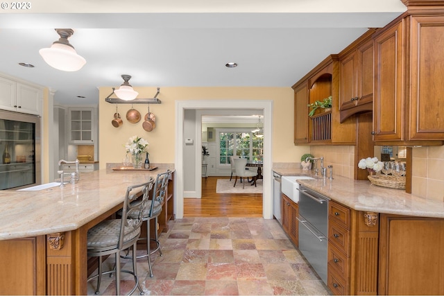 kitchen featuring kitchen peninsula, backsplash, light hardwood / wood-style flooring, dishwasher, and a breakfast bar area