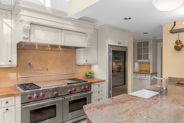 kitchen featuring white cabinetry, sink, double oven range, light stone counters, and tasteful backsplash