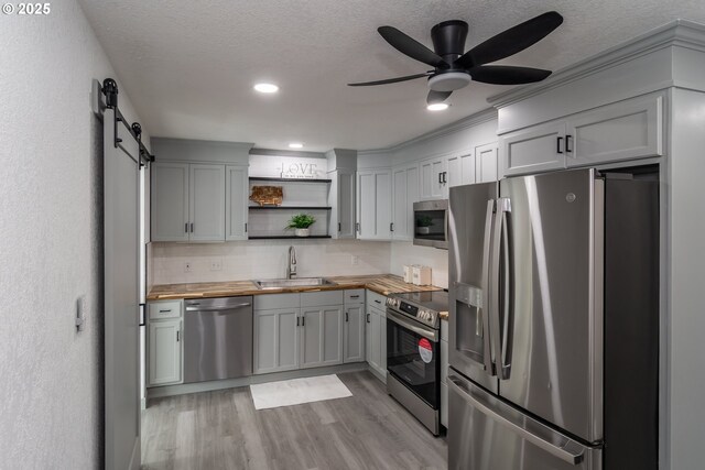 kitchen with open shelves, light wood-type flooring, a sink, stainless steel appliances, and butcher block countertops