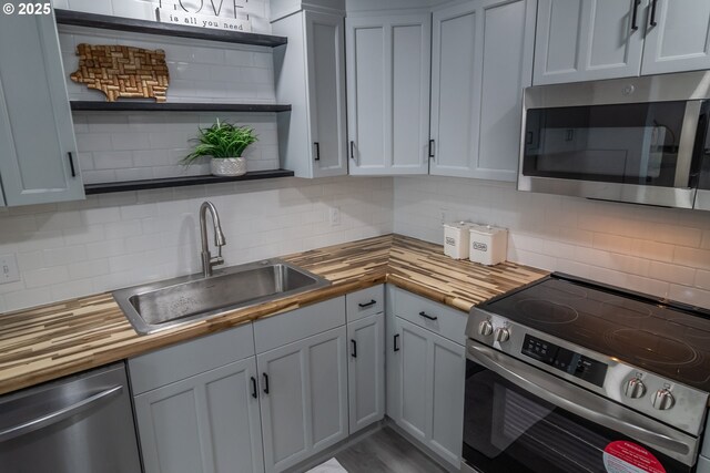 kitchen featuring open shelves, appliances with stainless steel finishes, a sink, backsplash, and butcher block counters