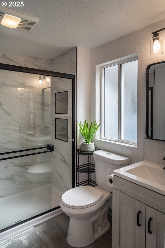 full bath featuring vanity, toilet, a textured ceiling, a shower stall, and visible vents