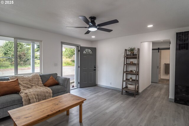 living room with ceiling fan, light wood-type flooring, a barn door, and a heating unit