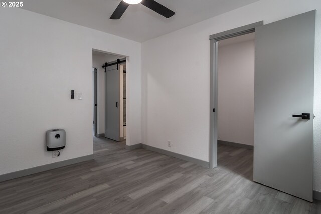 unfurnished bedroom with a barn door, baseboards, ceiling fan, and wood finished floors