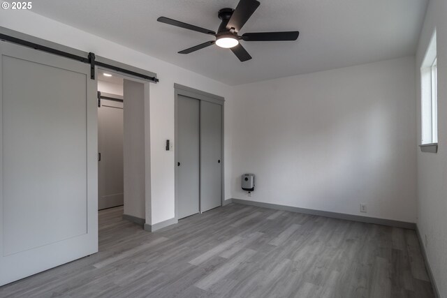 unfurnished bedroom featuring light wood-type flooring, a barn door, baseboards, and a ceiling fan