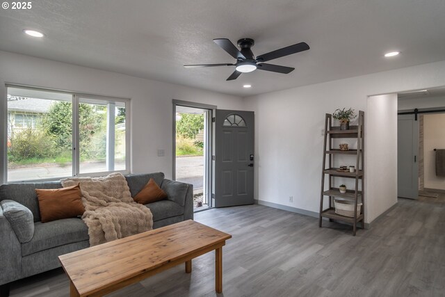 living area featuring recessed lighting, ceiling fan, a barn door, and light wood-type flooring