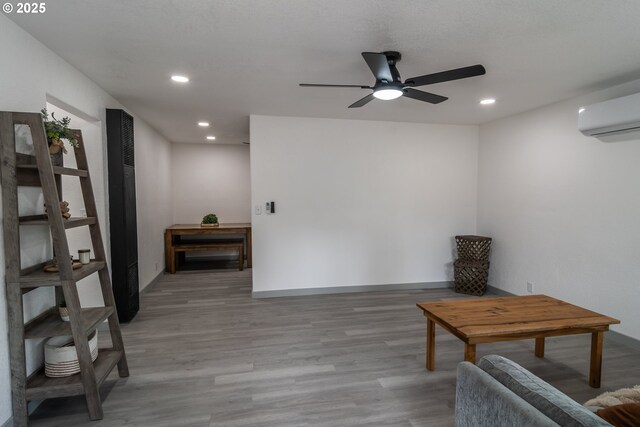 living area with ceiling fan, baseboards, an AC wall unit, recessed lighting, and light wood-style flooring