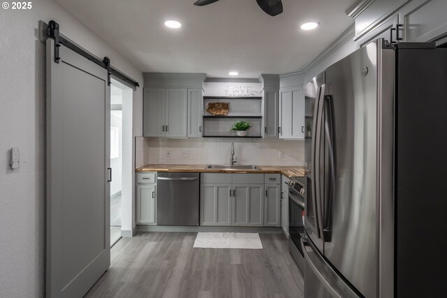 kitchen with open shelves, a barn door, a sink, butcher block countertops, and stainless steel appliances