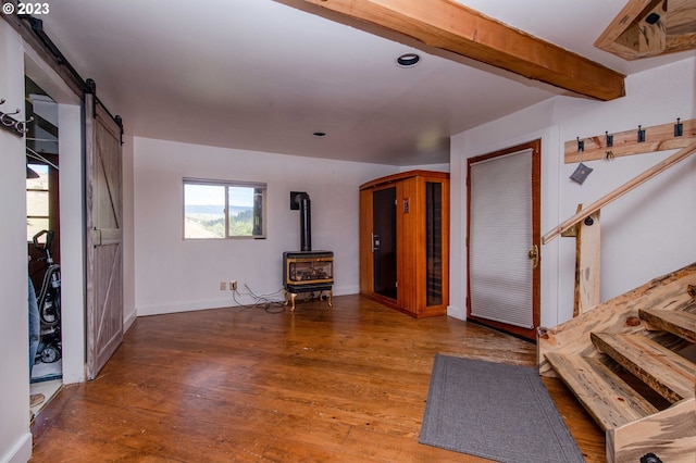 interior space featuring a barn door, a wood stove, dark hardwood / wood-style floors, and beam ceiling