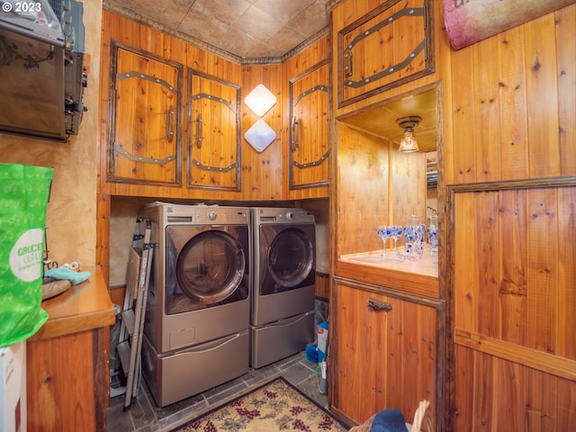 laundry room featuring wood walls, dark tile flooring, cabinets, and washer and clothes dryer