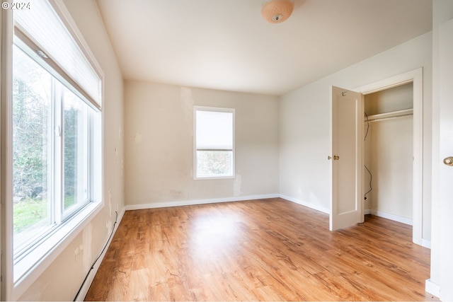 unfurnished bedroom with light wood-type flooring, a closet, and multiple windows