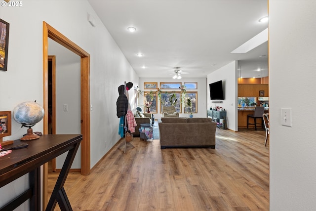 living room featuring ceiling fan, light wood-type flooring, and a skylight