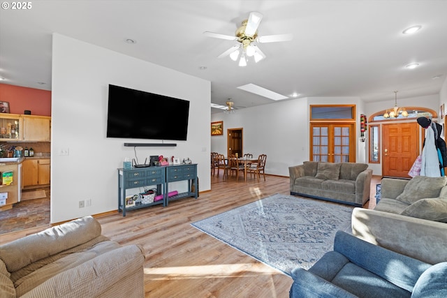 living room featuring wood-type flooring, a skylight, and ceiling fan with notable chandelier