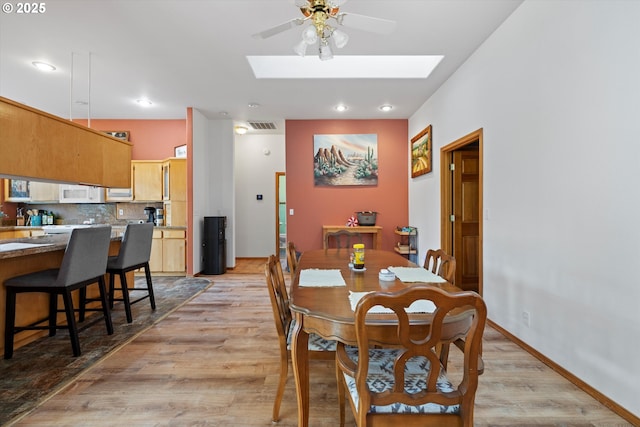 dining area with ceiling fan, a skylight, and light hardwood / wood-style flooring