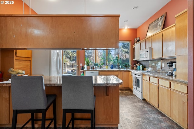 kitchen with white appliances, tasteful backsplash, kitchen peninsula, light stone counters, and a breakfast bar